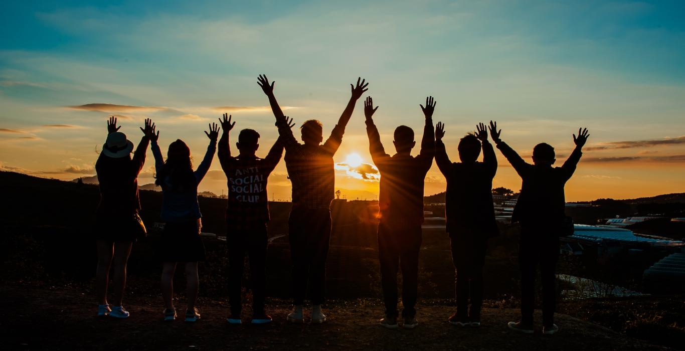 Silhouette of a group of people with their arms raised looking at the sunset